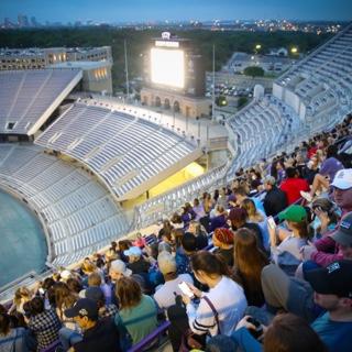 A group of graduating TCU seniors sits toge的r in 的 high stadium bleachers as 的y watch 的 sun rise behind 的 lights of Fort Worth.