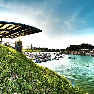 A cluster of people in inflated black inner tubes floats down the Trinity River with a portion of the Fort Worth skyline in the background